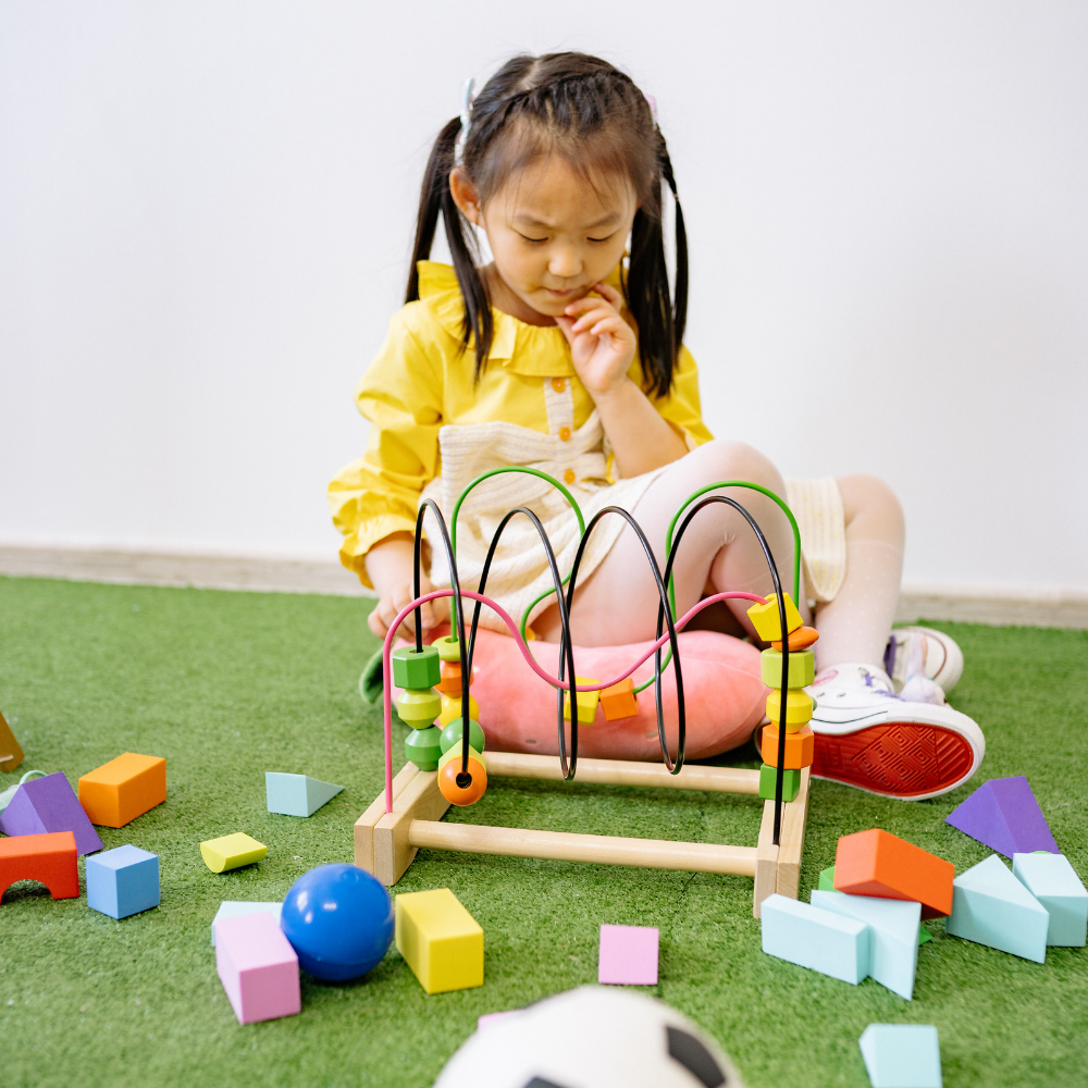 Child playing with a colorful toy on a green floor

