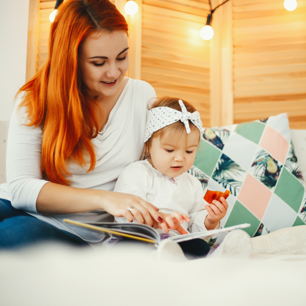 Woman and child reading a book together on a bed with warm lighting

