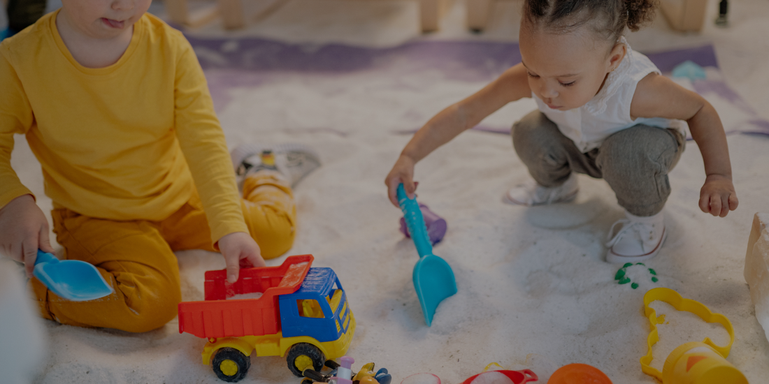 Two children playing with toys in a sand pit.

